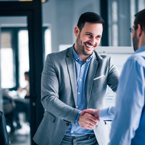 two-smiling-businessmen-shaking-hands-while-standing-office